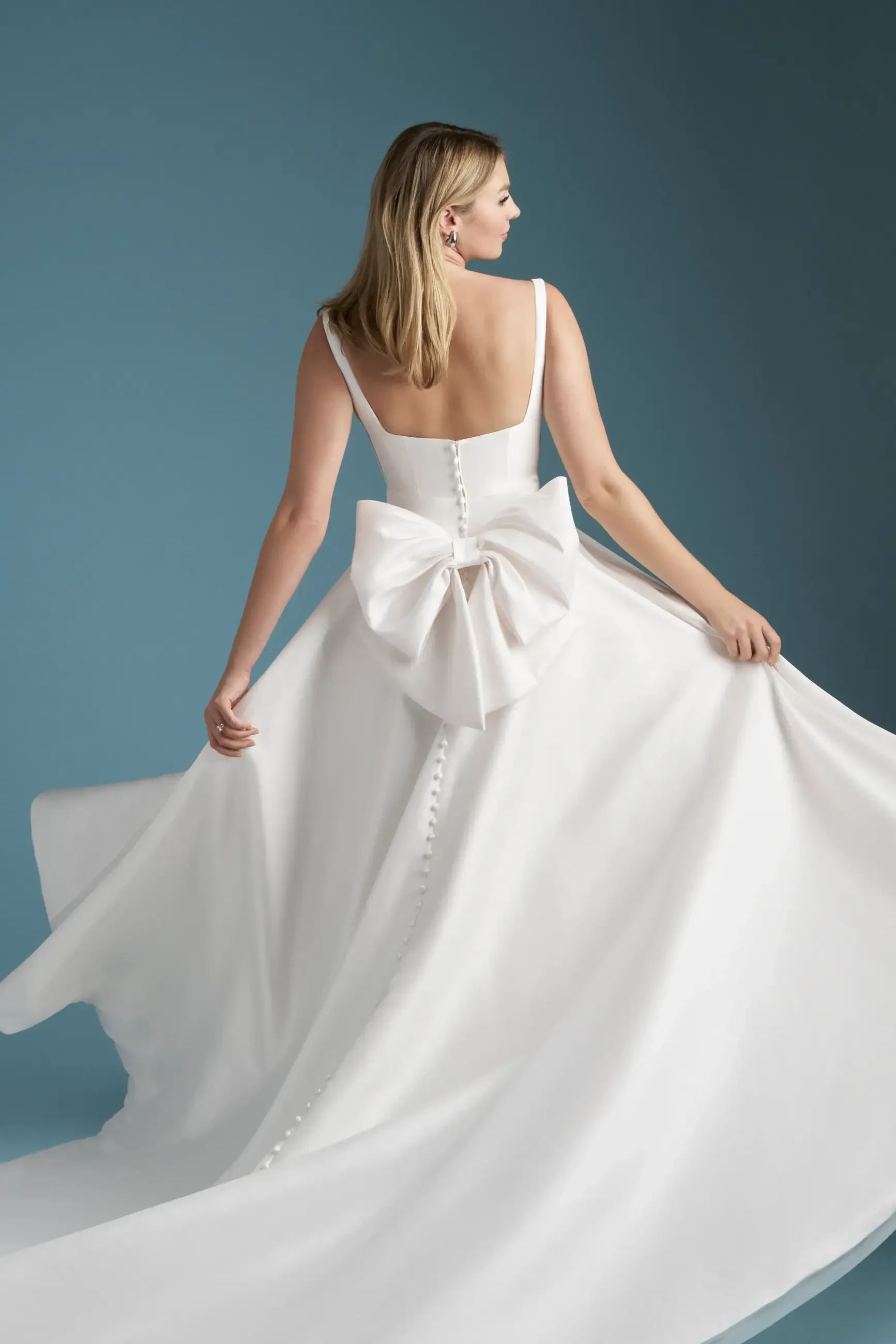 Model is wearing a Mikado ballgown with a scoop neckline, delicate spaghetti straps, and a detachable bow at the back.