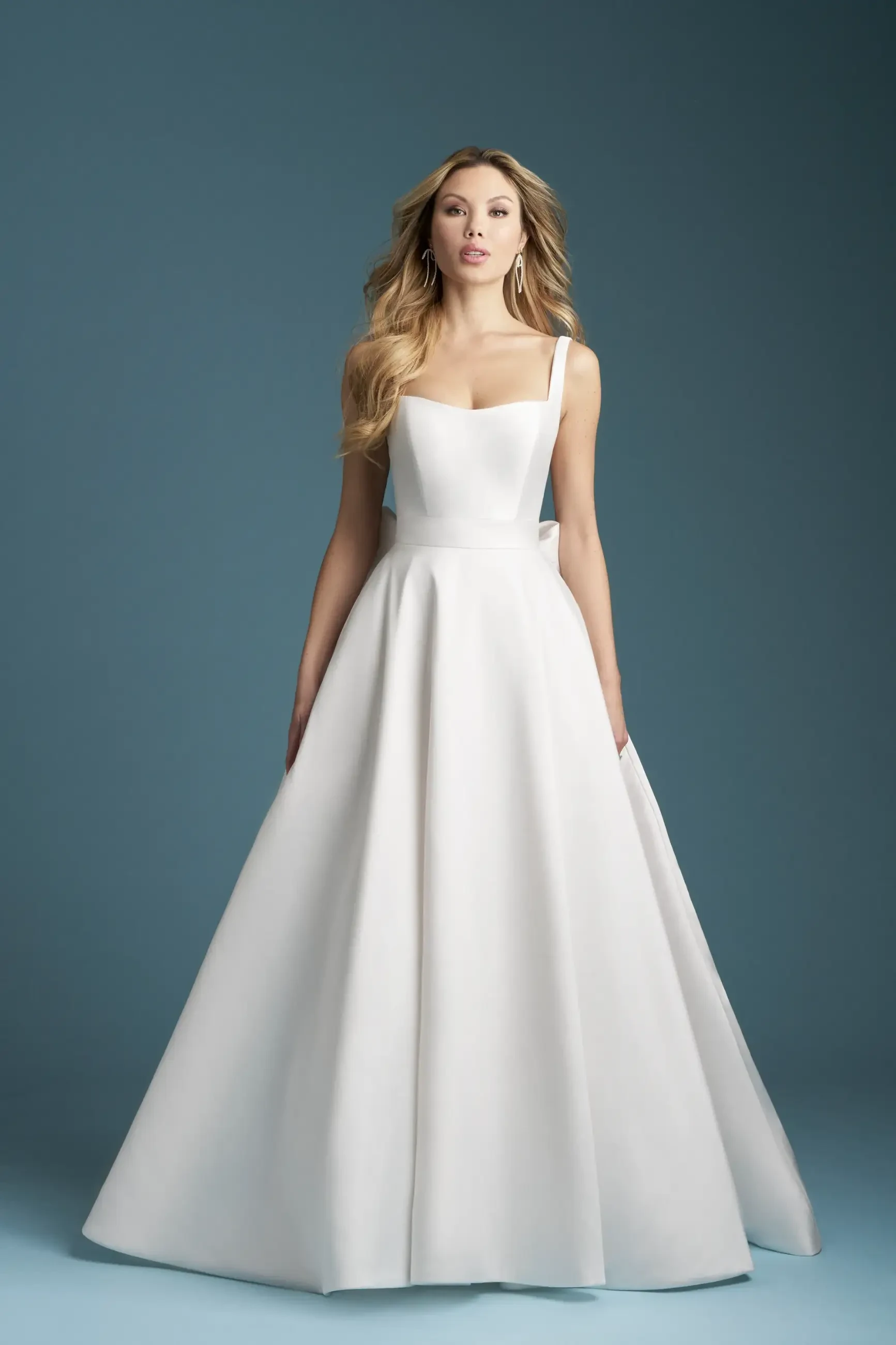 Model is wearing a Mikado ballgown with a scoop neckline, delicate spaghetti straps, and a detachable bow at the back.