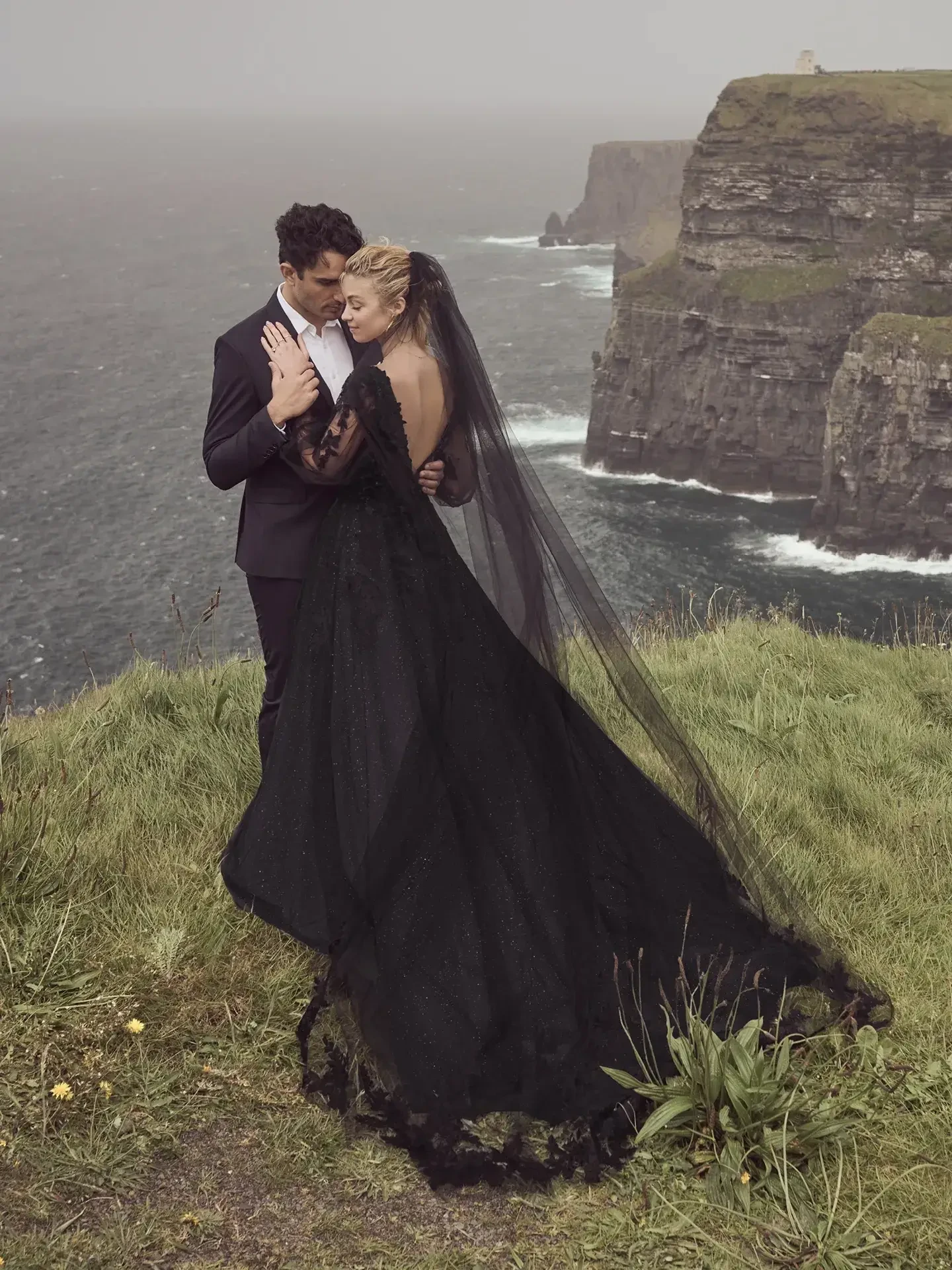 Model is wearing an A-line wedding dress with a flowing tulle skirt, floral lace details, and illusion bishop sleeves.
