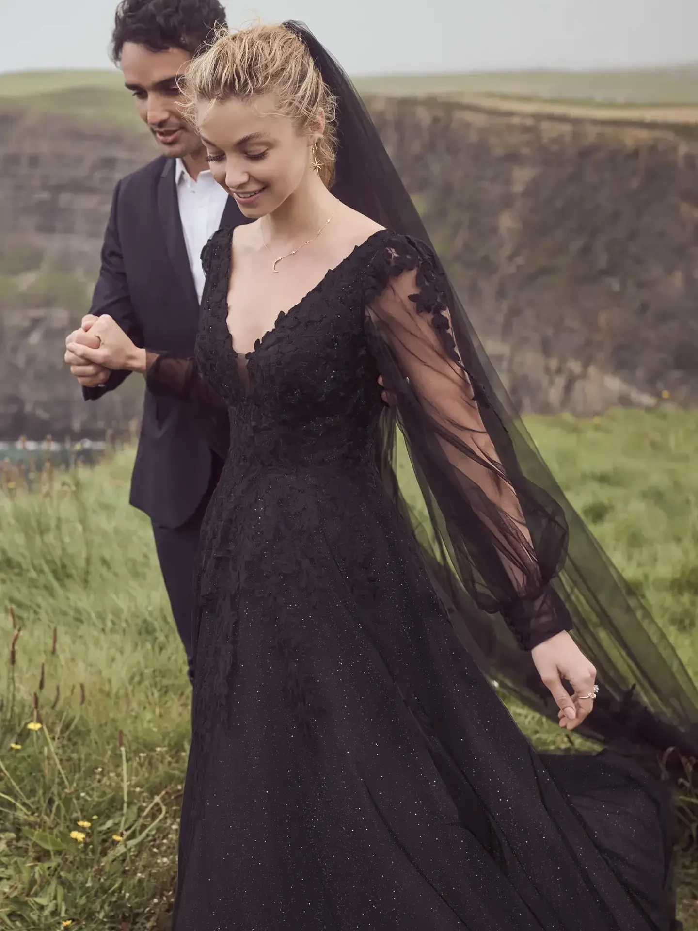 Model is wearing an A-line wedding dress with a flowing tulle skirt, floral lace details, and illusion bishop sleeves.
