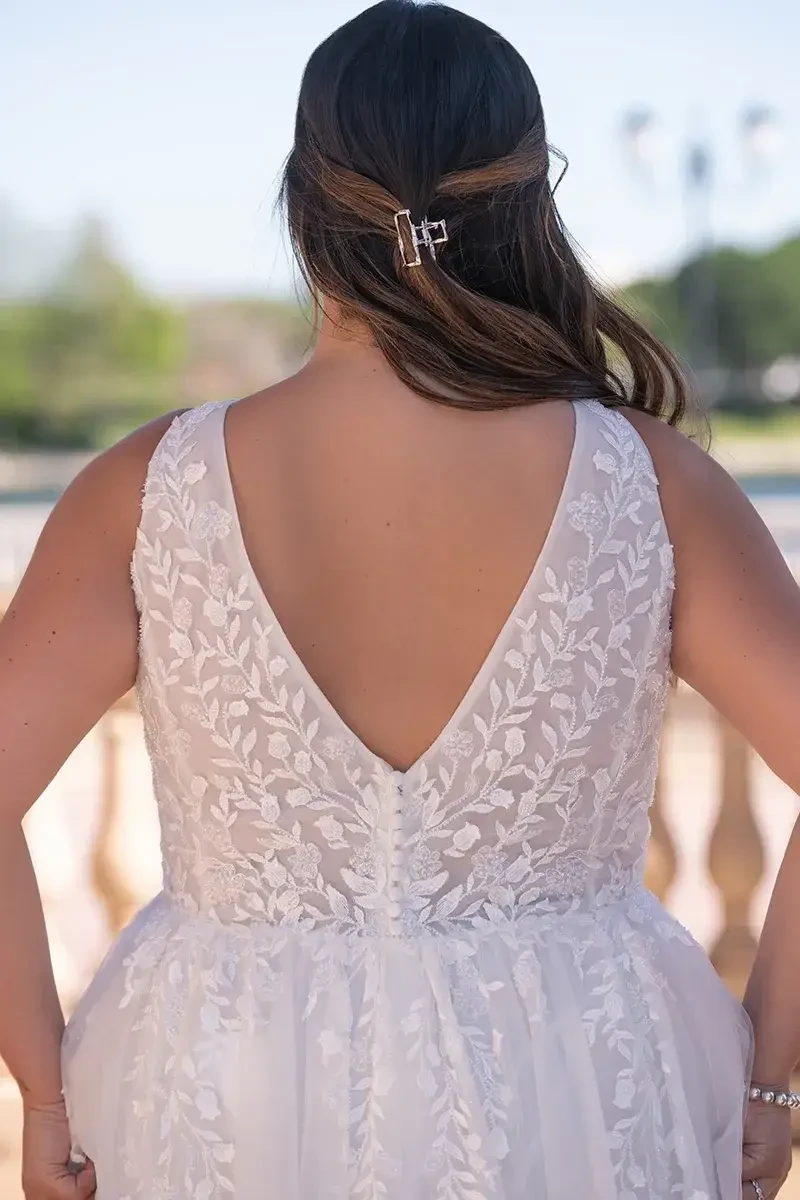 Model is wearing a soft A-line lace gown with a plunging neckline and sleeveless bodice.