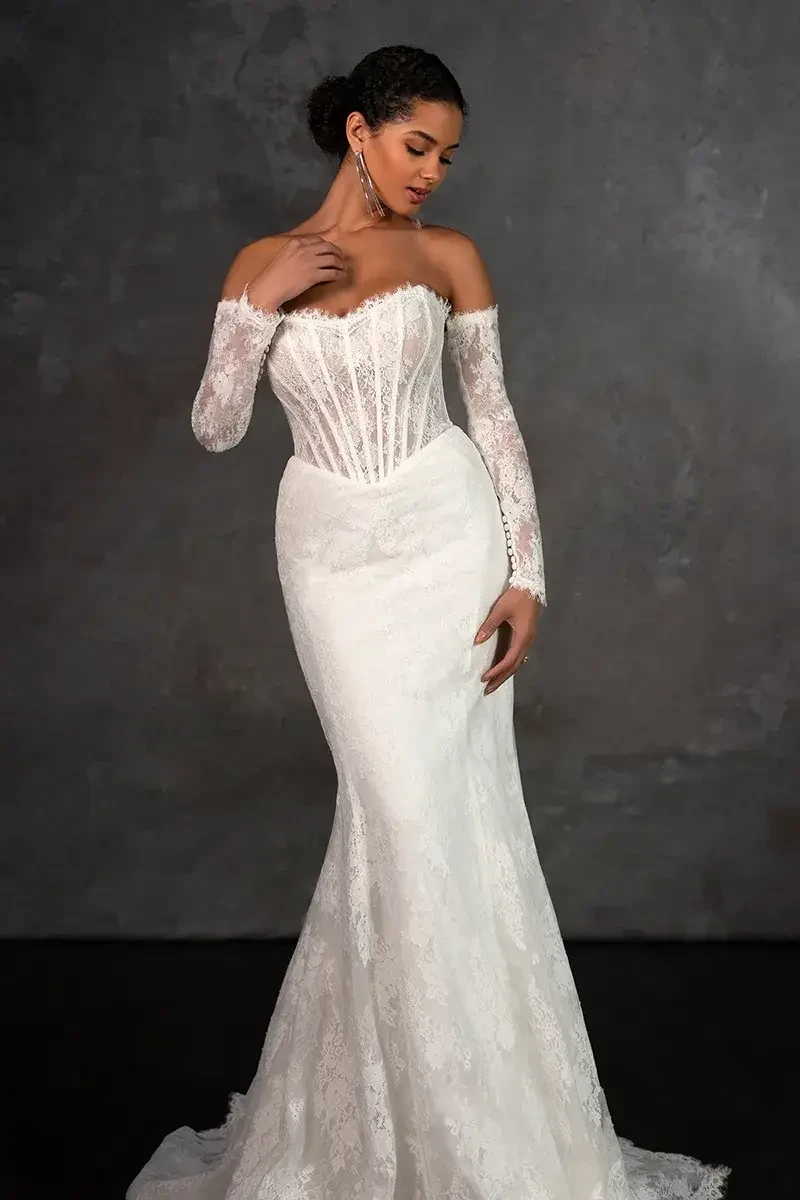Model is wearing a strapless Chantilly lace column gown with a sweetheart neckline, exposed boning, and detachable sheer lace sleeves.