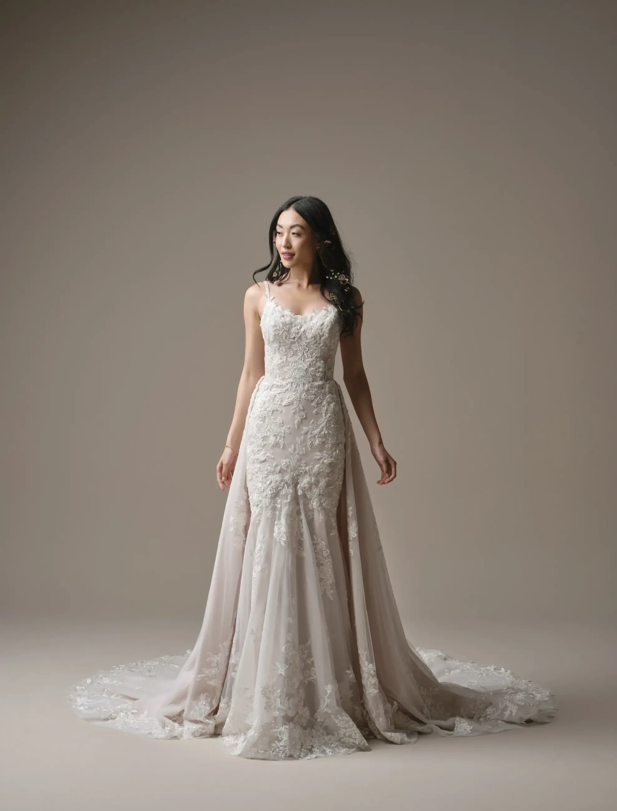 A woman is wearing a beautiful, intricately designed gown with lace and embellishments, standing gracefully against a neutral background.